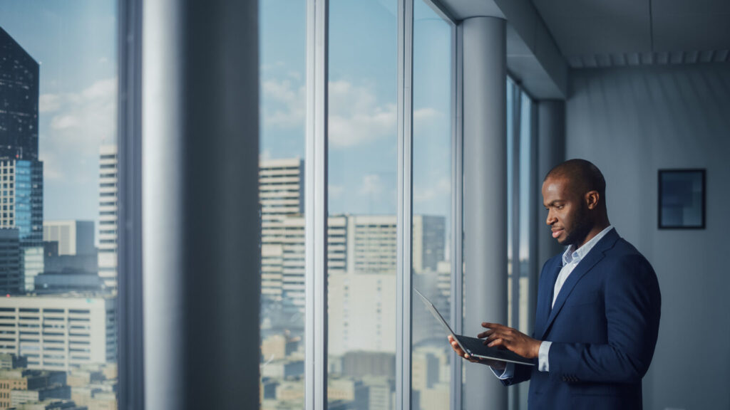 Thoughtful Black Businessman in a Tailored Suit Using Laptop whi